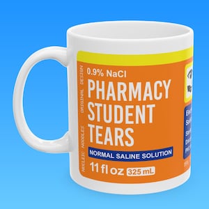 May include: White ceramic mug with a yellow and orange label that reads "0.9% NaCl Pharmacy Student Tears Normal Saline Solution 11 fl oz 325 mL".