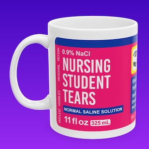 May include: White ceramic mug with a pink and blue label that reads "0.9% NaCl Nursing Student Tears Normal Saline Solution 11 fl oz 325 mL".