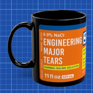 May include: Black ceramic mug with a white label that reads "0.9% NaCl Engineering Major Tears Normal Saline Solution 11 fl oz 325 mL". The label has orange and blue text.
