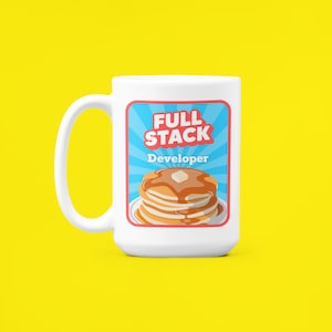 K&ouml;nnte beinhalten: Wei&szlig;e Keramiktasse mit einer blauen, roten und wei&szlig;en Grafik eines Stapels Pfannkuchen mit Sirup und einer Butterflocke. Die Grafik lautet "Full Stack Developer" in roten und wei&szlig;en Buchstaben.