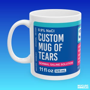 May include: White ceramic mug with a blue label that reads "CUSTOM MUG OF TEARS" with "NORMAL SALINE SOLUTION" and "325 mL". The mug has a curved handle and the text "0.9% NaCl" is also visible. The mug holds 11 fl oz.