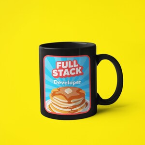 K&ouml;nnte beinhalten: Schwarze Kaffeetasse mit einer wei&szlig;en Grafik eines Stapels Pfannkuchen und dem Text "Full Stack Developer".