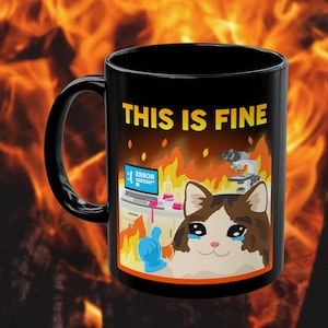 May include: Black ceramic mug with the phrase "THIS IS FINE" in yellow. The mug features a cartoon cat in a room on fire, with a laptop displaying an error message and laboratory equipment.