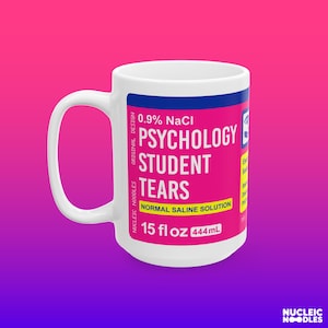 May include: White ceramic mug with a pink and blue label that reads "0.9% NaCl Psychology Student Tears Normal Saline Solution 15 fl oz 444mL".