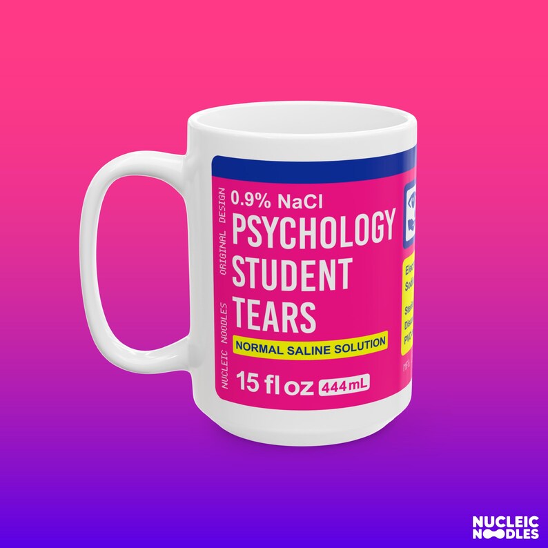May include: White ceramic mug with a pink and blue label that reads "0.9% NaCl Psychology Student Tears Normal Saline Solution 15 fl oz 444mL".