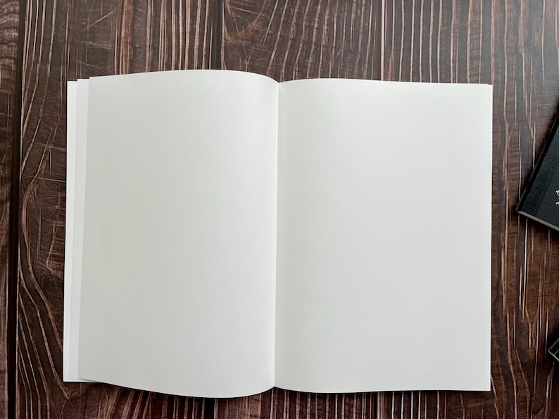 May include: A blank, white notebook with a hard cover, open to a fresh, empty page. The notebook is lying flat on a dark brown wooden surface.