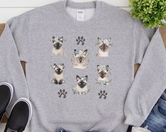 May include: Gray sweatshirt with a print of six Siamese cats wearing flower crowns. Each cat is surrounded by a floral design. The sweatshirt also has two paw prints on the bottom.