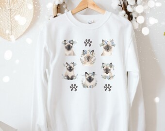 May include: White sweatshirt with a graphic print of seven Siamese cats wearing flower crowns. The cats are arranged in a grid pattern with paw prints in the corners.