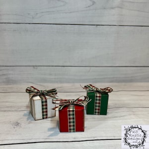 Könnte beinhalten: Drei kleine Geschenkkisten aus Holz mit rotem, grünem und weißem kariertem Band. Die Kisten sind mit einem Kalkwascheffekt verziert.