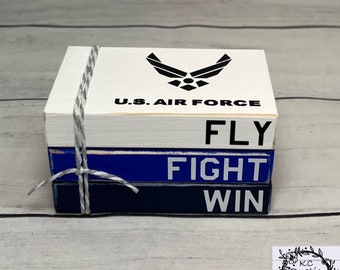 May include: A three-tiered wooden block set with the words "FLY", "FIGHT", and "WIN" in white lettering. The top block features the U.S. Air Force logo and the words "U.S. AIR FORCE" in black lettering.