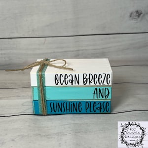 May include: Stacked wooden blocks painted in shades of blue and white with the text "ocean breeze and sunshine please" in black lettering. The blocks are tied together with twine.