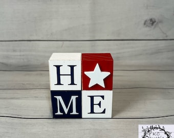 May include: Wooden block sign spelling "HOME" with a red, white and blue colour scheme. The "O" is replaced with a white star on a red background.