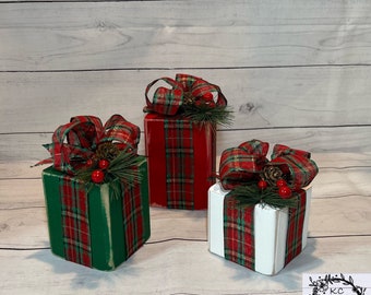 May include: Three wooden gift boxes decorated with red and green plaid ribbon, pine sprigs, and red berries. The boxes are painted in red, green, and white.