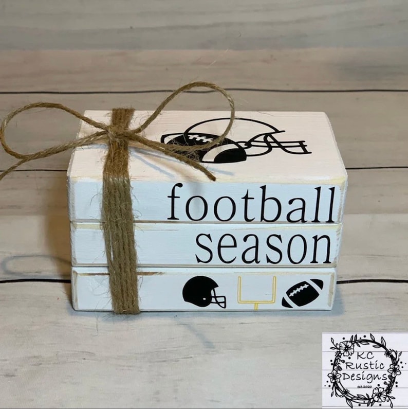 May include: A stack of three white wooden blocks with black and yellow football-themed designs. The top block has a football helmet and the words "football season" on the front. The bottom block has a football helmet, football, and goal post.