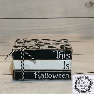 Peut inclure: Une pile de trois blocs de bois décoratifs attachés avec de la ficelle noire et blanche. Le bloc supérieur présente un motif Jack Skellington. Le bloc du milieu est blanc et le bloc inférieur indique "Halloween".