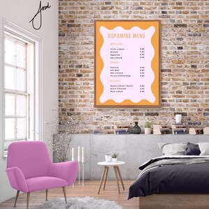 May include: A framed poster with a pink and orange background. The poster has the title "Dopamine Menu" and lists activities with prices. The poster is hanging on a brick wall in a room with a pink armchair, a white side table, and a bed with a gray duvet.