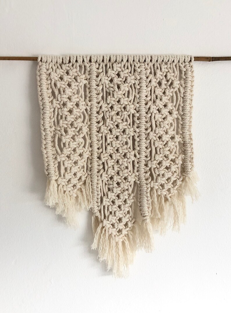 May include: A beige macrame wall hanging with a geometric pattern and fringe details.