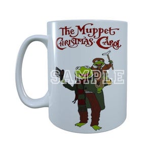 Puede incluir: Taza de cerámica blanca con una colorida ilustración de personajes de The Muppet Christmas Carol. La taza tiene un asa grande y el título de la película está impreso en rojo.