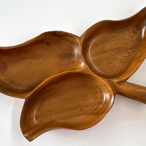 May include: A wooden serving tray with three separate compartments, shaped like a leaf with a handle. The tray is made of dark brown wood and has a natural finish.