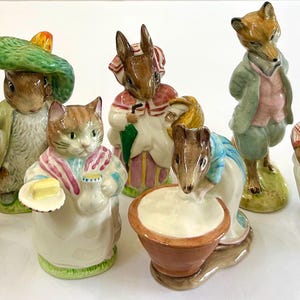 May include: A collection of ceramic figurines depicting anthropomorphic animals. The figurines include a cat, rabbit, fox, and mouse, each dressed in detailed clothing and accessories. The color palette includes soft pastels and earth tones.