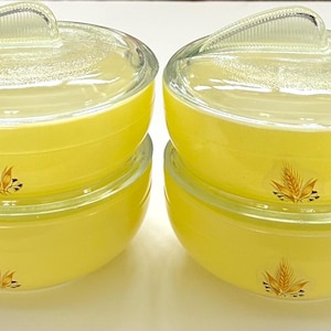 May include: Four vintage yellow glass soup bowls with clear glass lids and yellow handles. Each bowl features a wheat design. The bowls are stacked in pairs, showcasing their design and functionality. A classic kitchenware set.