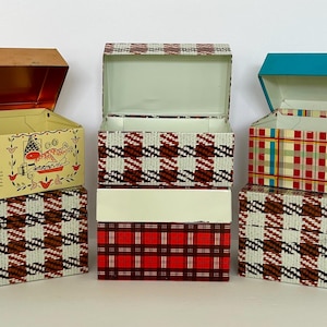May include: Five rectangular metal storage tins with hinged lids. One tin features a cream background with an onion soup recipe and illustrations. The other four tins display various plaid patterns in red, white, brown, and teal color schemes.