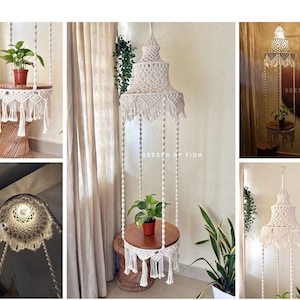 Puede incluir: Colgador de plantas de macramé blanco roto con una estantería de madera que sostiene una planta en maceta. El diseño de macramé presenta intrincados nudos y flecos. El texto "SEESEE BY FIDA" es visible.