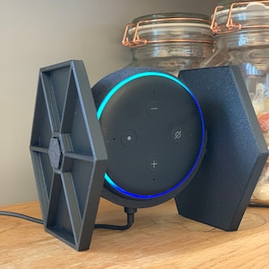 Peut inclure: Un support imprimé en 3D noir en forme de vaisseau spatial Tie Fighter de Star Wars, tenant un haut-parleur intelligent Amazon Echo Dot noir avec un anneau lumineux bleu autour du haut.
