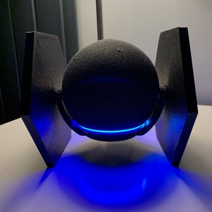 May include: A black spherical speaker with a blue light ring around the middle, mounted on a black stand with two wings.