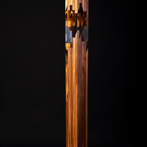 May include: A tall, wooden sculpture with a geometric design. The sculpture is made of multiple pieces of wood that are interlocked together. The wood is a rich brown color and has a natural grain pattern. The sculpture is standing on a wooden base.