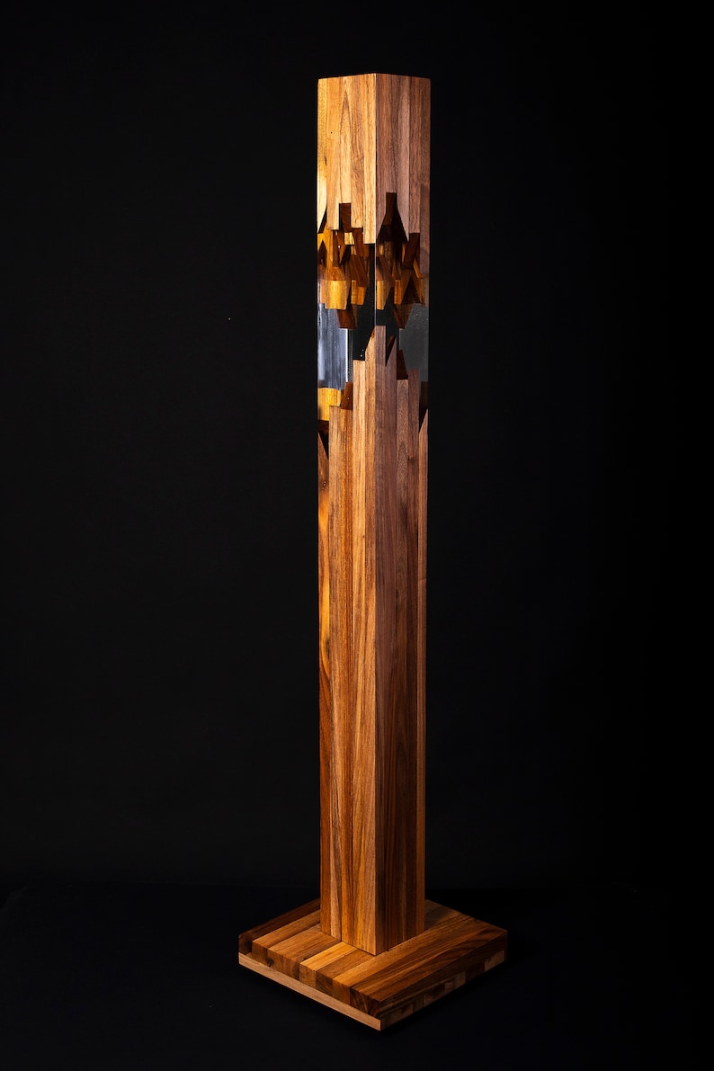 May include: A tall, wooden sculpture with a geometric design. The sculpture is made of multiple pieces of wood that are interlocked together. The wood is a rich brown color and has a natural grain pattern. The sculpture is standing on a wooden base.