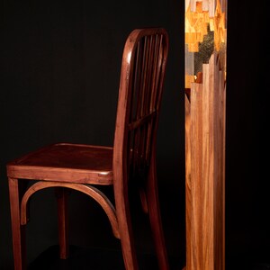 May include: A wooden chair with a dark brown finish sits next to a tall, wooden floor lamp. The lamp has a clear glass section in the middle with gold leaf accents.