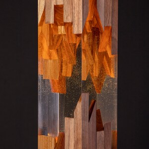 May include: A tall, rectangular wooden sculpture with a clear resin section in the middle. The resin is filled with small, golden flecks and the wood is a rich brown color.
