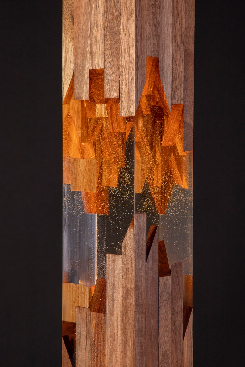 May include: A tall, rectangular wooden sculpture with a clear resin section in the middle. The resin is filled with small, golden flecks and the wood is a rich brown color.