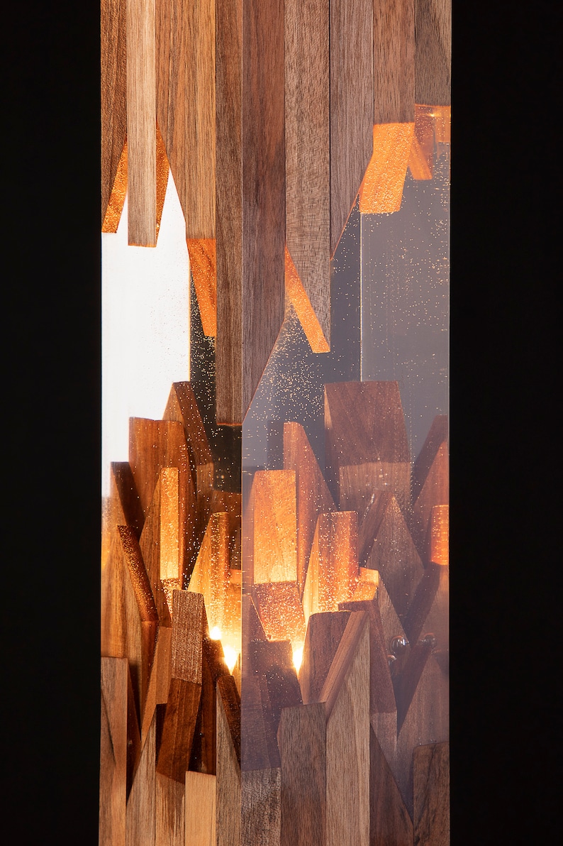 May include: A rectangular wooden lamp with a clear resin exterior. The wood is arranged in a geometric pattern and illuminated from within, creating a warm glow.