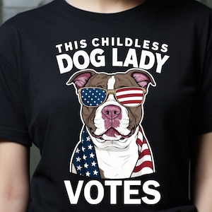 May include: Black t-shirt with a graphic of a dog wearing sunglasses and a scarf with the American flag. The text on the shirt reads "This Childless Dog Lady Votes".