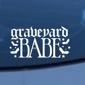 May include: White vinyl decal with the text "graveyard babe" in a gothic font. The text is surrounded by small bat silhouettes.