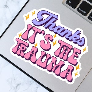Puede incluir: Una pegatina rosa y morada con el texto "Thanks It's The Trauma" en una fuente retro. La pegatina tiene estrellas doradas alrededor del texto.