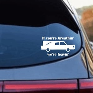 Peut inclure: Un autocollant en vinyle blanc sur une voiture bleue avec une silhouette de corbillard et le texte "If you're breathin' we're leavin'"