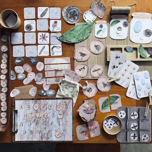May include: A selection of educational wooden toys and learning materials, including alphabet letters, number cards, and nature-themed illustrations. The set includes jars labelled "Small," "Medium," and "Big," along with wooden slices and cards. The colour palette is natural, with browns, greens, and whites.