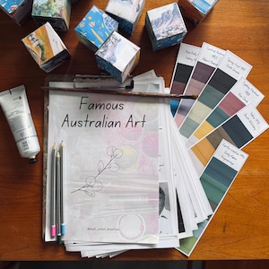 Può includere: Una composizione artistica con una lavagna con testo "Famous Australian Art", campioni di colore, matite, un tubetto di vernice e cubi dipinti. I campioni di colore sono etichettati con nomi di artisti e anni. I cubi sono decorati con immagini colorate.