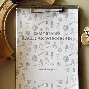 Może przedstawiać: Klip z "Race Car Workbook" dla początkujących czytelników, z powtarzającym się wzorem części samochodowych, znajduje się w drewnianym torze kolejki zabawki. Mały szary samochodzik spoczywa na torze.