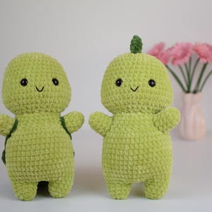 Op de afbeelding: Twee groene gehaakte schildpad knuffels met lachende gezichten. De schildpad links heeft een schild, terwijl de schildpad rechts een puntige kop heeft.