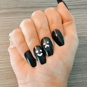 Könnte beinhalten: Schwarze Sargnagel mit weißen Smiley- und traurigen Gesichtsdesigns.