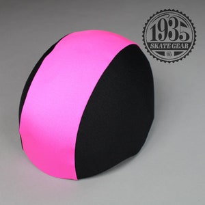 Puede incluir: Un casco rosa y negro con un acabado liso y brillante. El casco está diseñado para el skateboarding y otros deportes de acción.