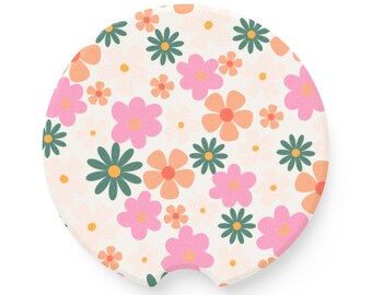 May include: A round, white car coaster with a pattern of pink, orange, and green flowers. The coaster has a cut-out shape for a cup.