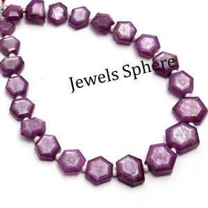 May include: A strand of purple gemstone beads with a faceted hexagonal shape. The beads are strung on a silver wire and have a subtle shimmer. The strand is finished with red tassels.
