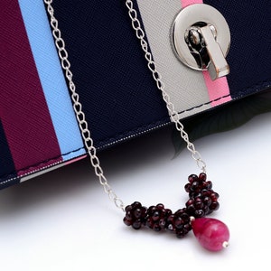 Op de afbeelding: Een zilveren ketting met een hanger gemaakt van rode granaatsteen en een traanvormige roze steen.