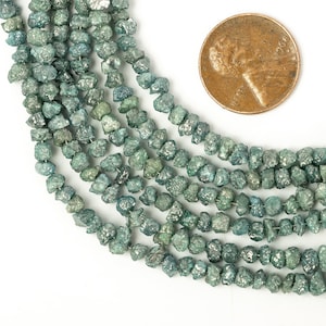 Pode incluir: Um fio de contas de diamante bruto, verdes e facetadas. As contas são de forma irregular e têm um aspeto natural e não polido. As contas são enfiadas num fio fino e têm aproximadamente 4 mm de diâmetro.