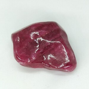 Puede incluir: Una piedra preciosa de color rojo intenso, de forma irregular, con una superficie lisa y pulida.